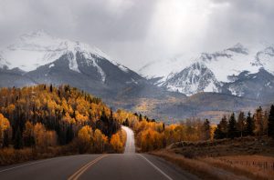Light rays shine down on a scenic road in Colorado surrounded by mountains and fall colors.